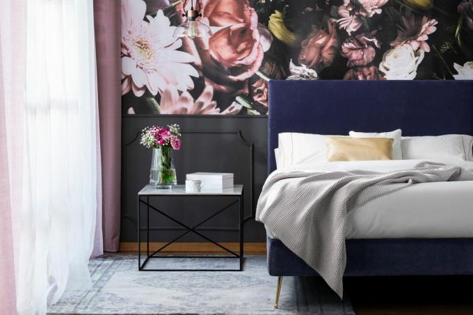 Bloemenmuurschildering in groene slaapkamer met blauw gestoffeerd bed, grijze plaid en laagpolig vloerkleed