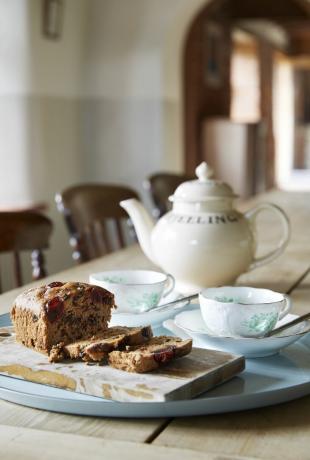 भोजन कक्ष में लकड़ी की मेज पर चाय के कप और चायदानी के साथ केक