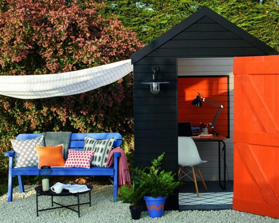 Schwarz gestrichener Schuppen mit leuchtend orangefarbener Innenausstattung und Gartenbank im Freien mit Kissen