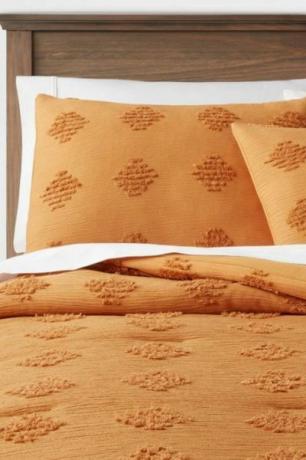 ผ้าปูที่นอนสีส้มประดับเพชรกระจุกบนเตียงสีขาวและโครงเตียงไม้ 