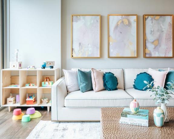 Sala de estar con sofá, arte de pared enmarcado e idea para guardar juguetes.