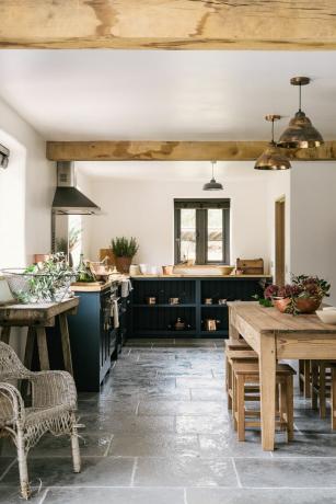ダークブルーのキャビネット、木製のダイニングテーブル、木製の調理台を備えたカントリーキッチンの石の床