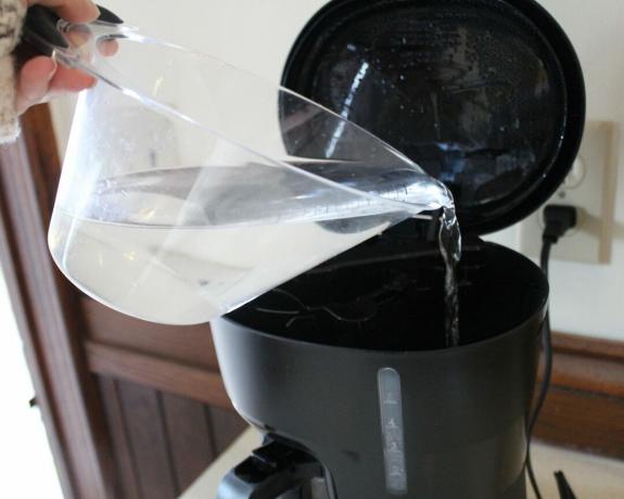 Camryn Rabideau vult Mr. Coffee druppelfilter koffiezetapparaat met water uit plastic maatbeker