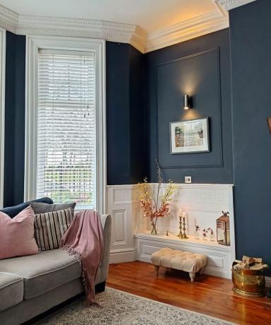 Hoek van woonkamer met roze fauteuil marineblauwe muren en een deel van een erker