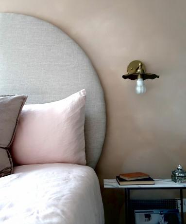 Cabeceira circular neutra em frente à parede do quarto rosa pálido