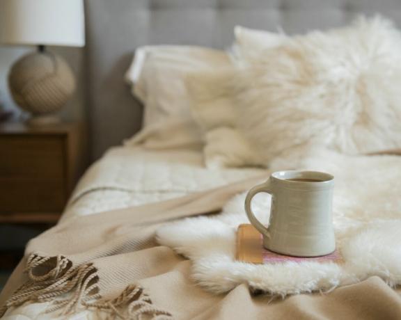 uma cama aconchegante com travesseiros felpudos e um cobertor e uma caneca ao pé da cama
