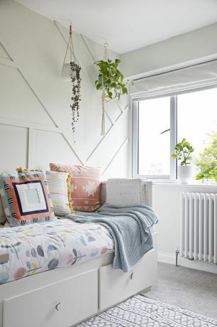 Cameră liberă cu pereți cu panouri geometrice albe, pat de zi alb și lenjerie de pat cu flori și perne multicolore