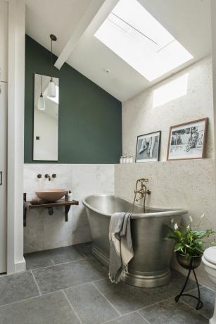 kaimiškas vonios kambarys su šlifuoto plieno ritinine vonia, plytelėmis išklotomis grindimis, akmens plokštėmis sienomis, sieniniu kriaukle, žaliai dažyta sienine palėpe
