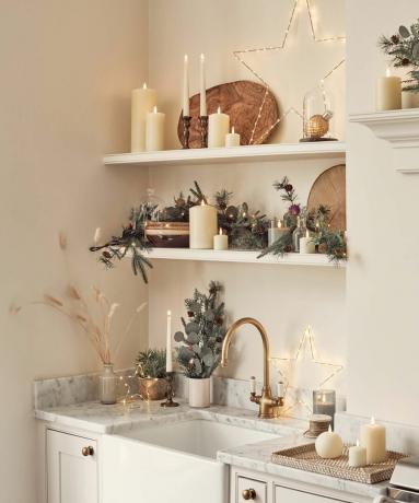 moderne kuhinjske police in pomivalno korito, okrašeno za božič z lučkami, listjem in stebričastimi svečami