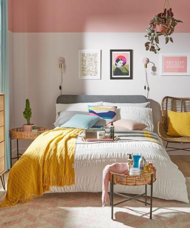 ห้องนอนทันสมัยตกแต่งด้วยกรอบผนัง ต้นไม้ในร่มแบบแขวน ผ้าคลุมสีเหลืองมัสตาร์ด และผนังสีชมพู