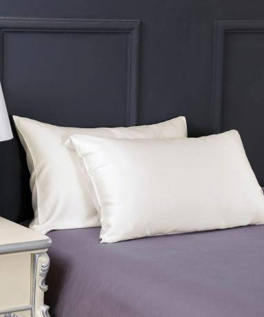 Kahest padjast koosnev komplekt, mis on ümbritsetud elevandiluust siidist padjapüüridega lilla voodikaunistusega voodil