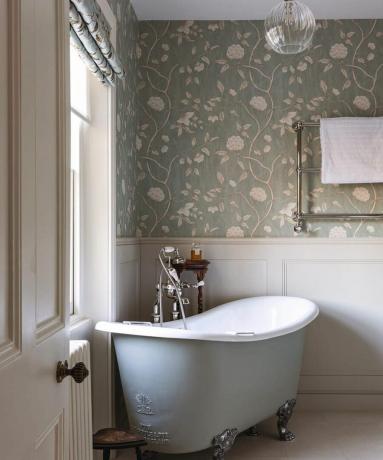 Hagyományos fürdőszoba zöld virágos tapétával, fehér falburkolattal és kis halványkék káddal