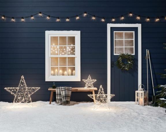 Decoración navideña al aire libre en una cabaña con tres estrellas iluminadas y luces de colores