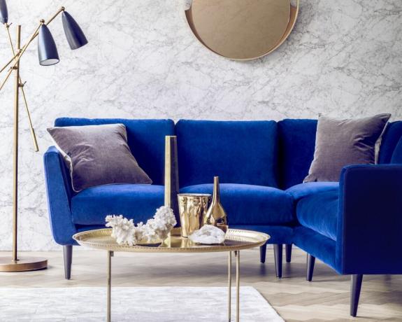 Небольшой угловой диван с синей бархатной обивкой в ​​гостиной с латунными аксессуарами
