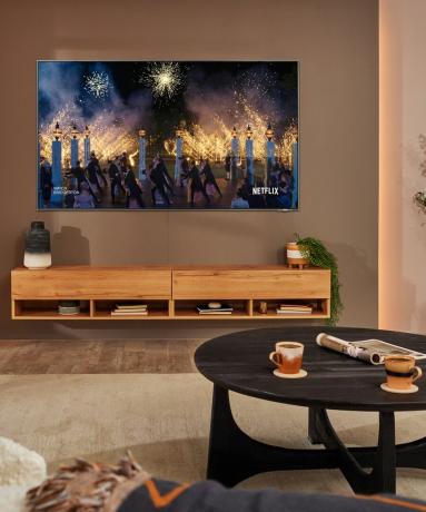 Зидни Самсунгов телевизор Тхе Фраме са дрвеним ормарићем, округлим столићем за кафу и декорацијом шољица за кафу