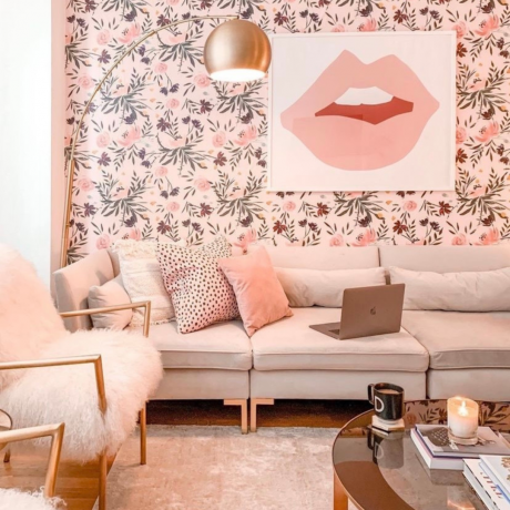 Esquema de sala de estar de blush suave com papel de parede floral moderno, arte de parede divertida, piso de casulo lamo e assentos táteis.
