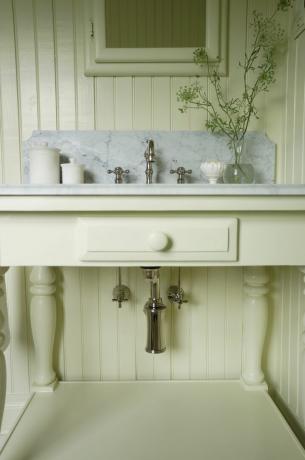 Upcyklingowana kremowa szafka łazienkowa w łazience z marmurowym blatem, srebrnymi akcentami i wiklinowymi koszami
