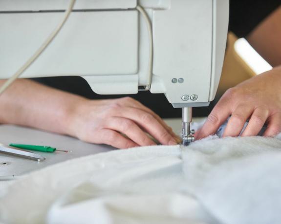mãos de mulher em uma máquina de costura, costurando tecido