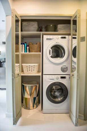 Hauswirtschaftsraum in einem Schrank mit Aufbewahrungskörben, gestapelter Waschmaschine und Trockner