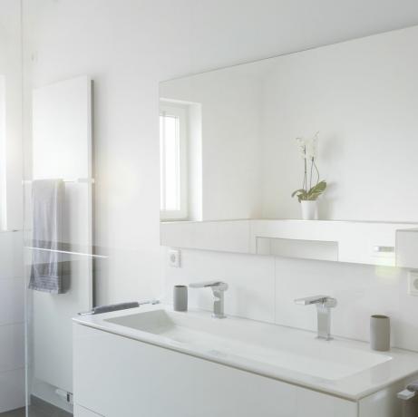 et helt hvidt badeværelse med håndvask og nærliggende bruser