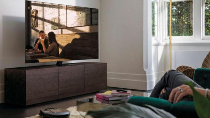 Samsung QN75Q80TAFXZA σε βάση τηλεόρασης απέναντι από καναπέ με παρακολούθηση τηλεόρασης