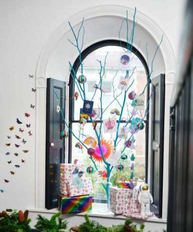забавна алтернативна идея за коледно дърво с пръскано клонче в прозореца и цветни украси, вдъхновени от разнообразието