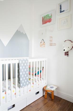 Gri boya ile duvarlarda beyaz karyola, beyaz duvarlar, kahverengi döşeme tahtaları ve dağ efektli desenli Scandi tarzı çocuk yatak odası