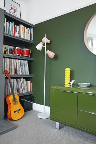 Ecke eines grauen Wohnzimmers mit grüner Wand, offenem Regal voller Schallplatten, grünem Sideboard und grauem Teppich