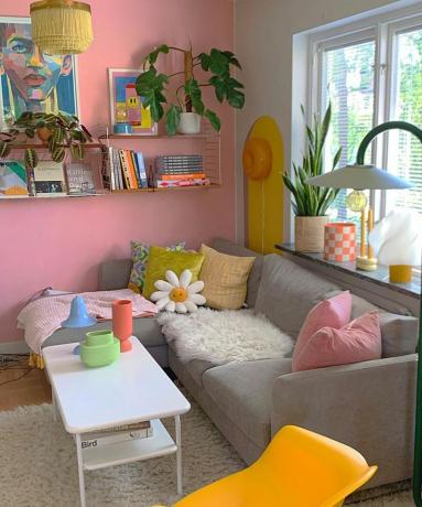 En farverig stue med en grå sofa, farverige hynder og dekorerede hylder
