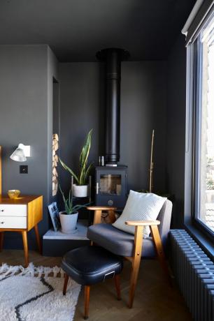 Jason Traves-huis: een donkere en humeurige zithoek in een omgebouwde loft met een fauteuil en voetenbank, een houtkachel en diepgrijs geverfde muren