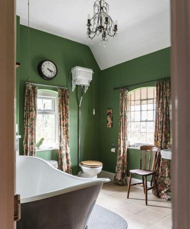 Un bagno con decorazioni in pittura murale verde, lunghe tende drappeggiate, lampadario e vasca da bagno color kaki