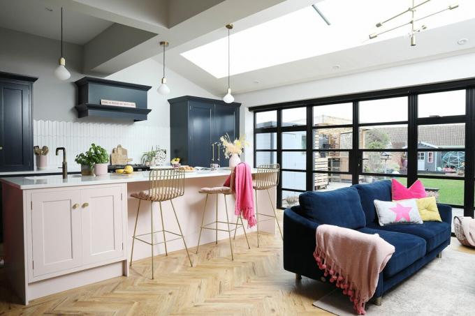 Cozinha com piso espinha de peixe, portas estilo Crittall, cozinha estilo Shaker azul escuro com ilha rosa claro e sofá de veludo azul