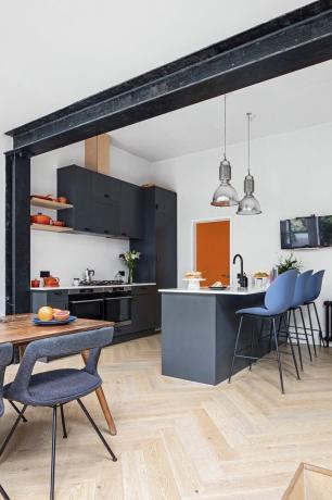 Cucina nera elegante con isola. Pavimenti in legno chevron, sgabelli da bar blu e lampade a sospensione in vetro sull'isola