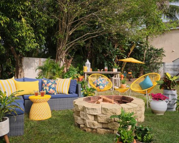 Dārzs ar pelēku dīvānu un dzelteniem spilveniem