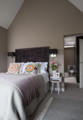 neutrales Schlafzimmer mit auffälligem Kopfteil, kräftigen Kissen, Wandleuchten und Nachttisch