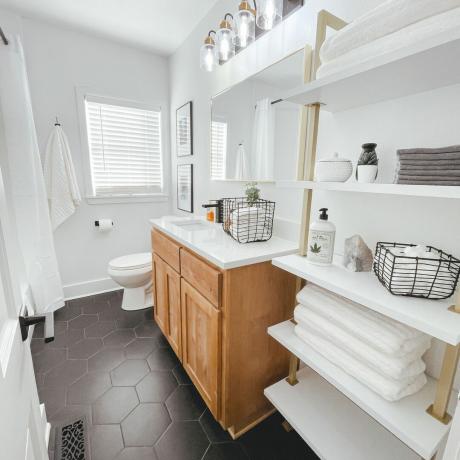 Banheiro de azulejo preto com armários brancos, toalhas e armário de madeira
