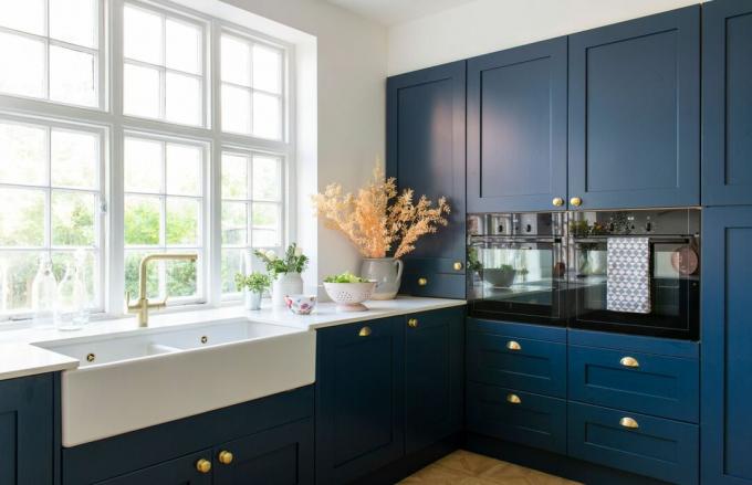 Tamsiai mėlyna virtuvė su žalvarinėmis rankenomis ir didele liokajaus kriaukle bei dideliu langu