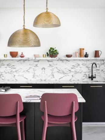 cucina in marmo con pendenti in oro, due sgabelli da bar rosa, ripiano in marmo