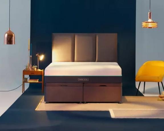 En madras, der ligger på en seng med en marineblå sengegavl i et moderne soveværelse