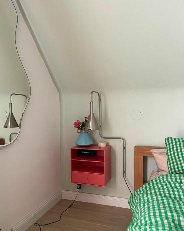 Uma cama verde ao lado de uma mesa de cabeceira rosa e um espelho