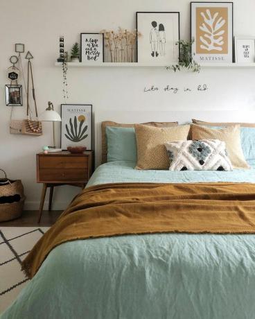 Un dormitor cu un pat albastru și maro, o noptieră și un raft de perete cu decorațiuni