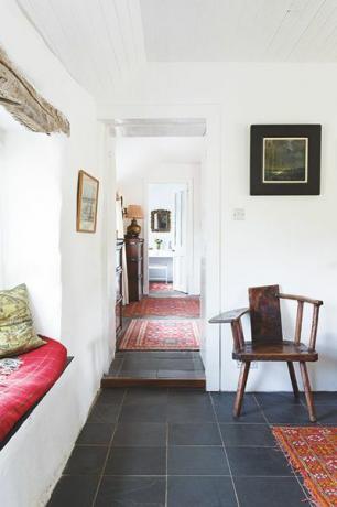 Ходник у приморском дому, са плочицама од шкриљевца, црвеним теписима, прозорским седиштем и старинском лулом и столицом
