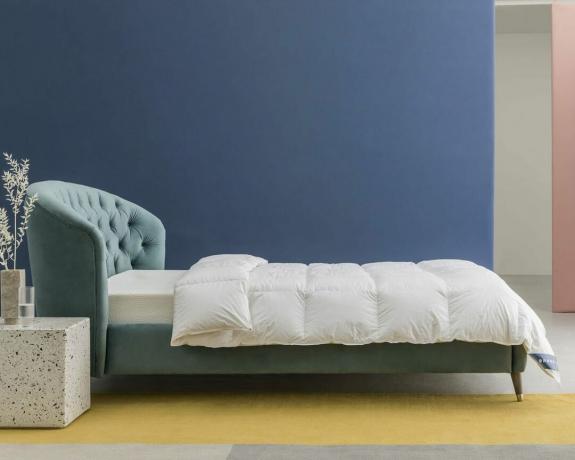 Un copripiumino in piuma d'oca adagiato su un letto con testiera in velluto verde acqua in una camera da letto blu contemporanea