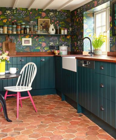 sekskantede terracotta gulvfliser i et blåt køkken med mønstret tapet og åbne hylder