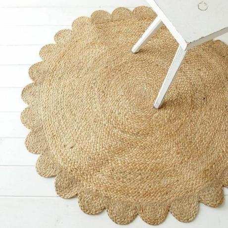 Um tapete circular de juta trançado com uma borda recortada exibido no chão sob uma cadeira de mesa de jantar branca. 