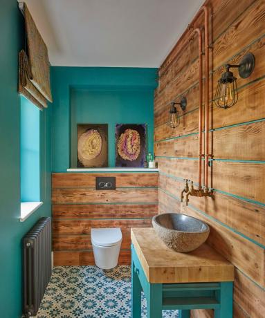 Ванна кімната, обшита синіми та дерев’яними панелями, із підлогою з плитки з синім візерунком та кам’яною раковиною