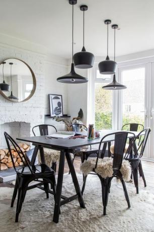 Nápady na závěsné světlo: jednobarevná jídelna s černým stolem a kovovými židlemi, kombinace černých závěsných světel v různých výškách, bíle natřená cihlová zeď a pod nimi bílý kožený koberec