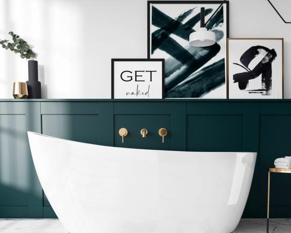 Ένα βαθύ πράσινο μπάνιο με λευκή μπανιέρα με παντόφλες και έργα τέχνης με πλαίσιο