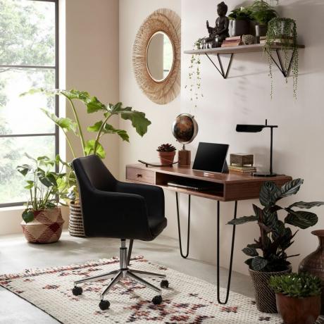 Jordnært hjemmekontor med skrivebord fra midten av århundret, jernben, ergonomisk stoffstol, teppe i berberstil og rottingspeil med dekorative stueplanter