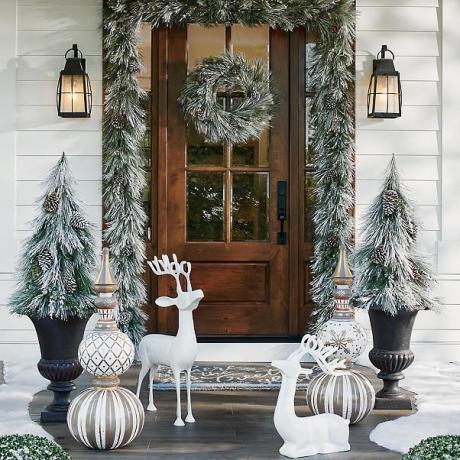 Decoración navideña al aire libre en un porche con follaje cubierto de nieve y árboles de Navidad